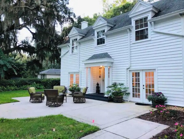 Une maison blanche à deux étages, dotée d’un patio couvert, de meubles d’extérieur et d’un jardin bien entretenu.