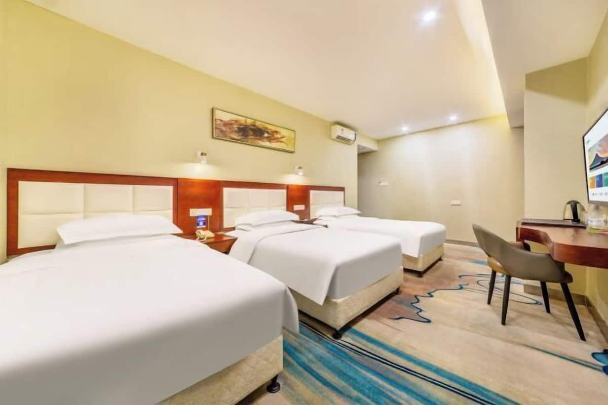 A hotel room with two beds, a desk, a chair, and a painting on the wall.