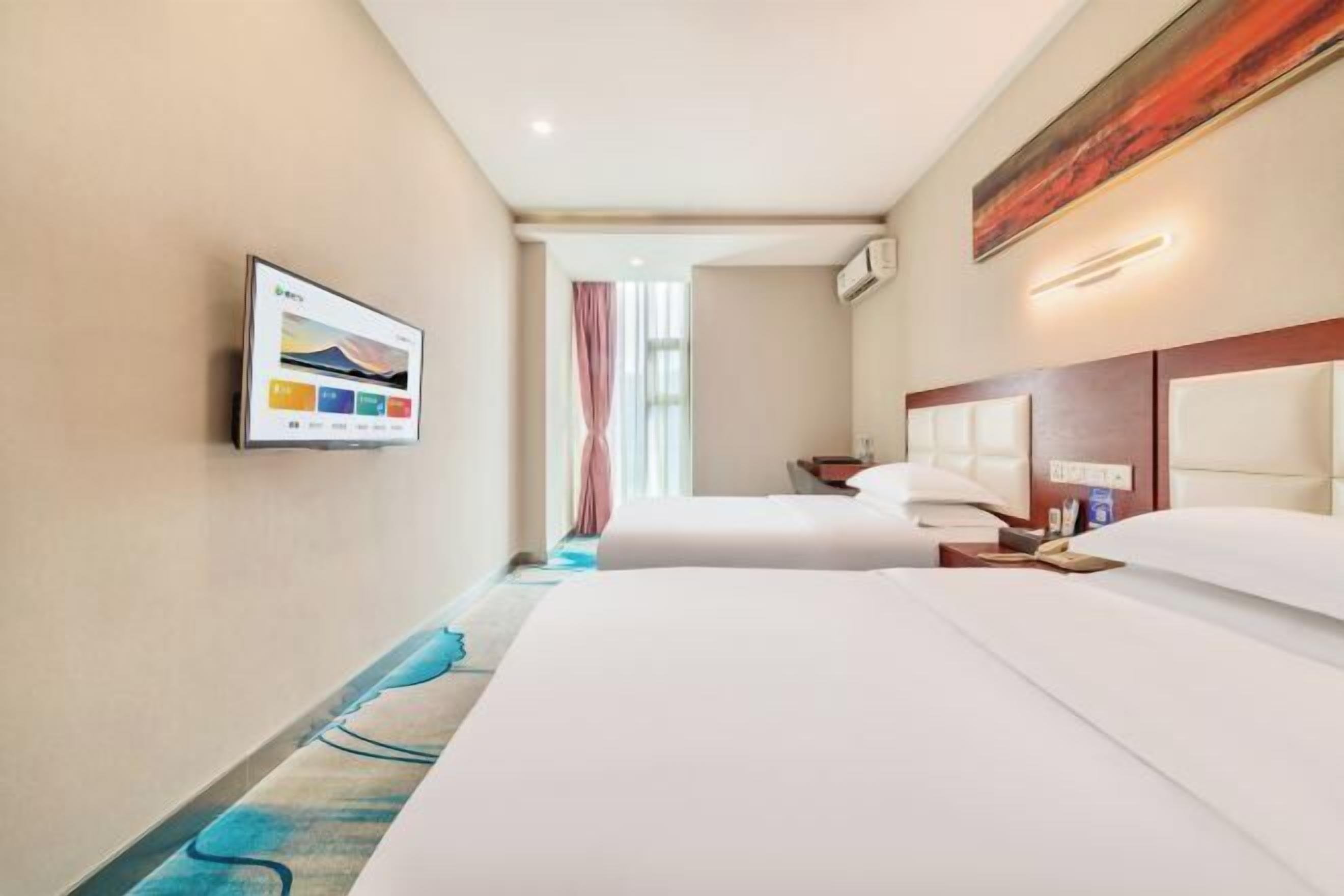 Une chambre d’hôtel avec deux lits, un téléviseur à écran plat fixé au mur et une fenêtre avec des rideaux.