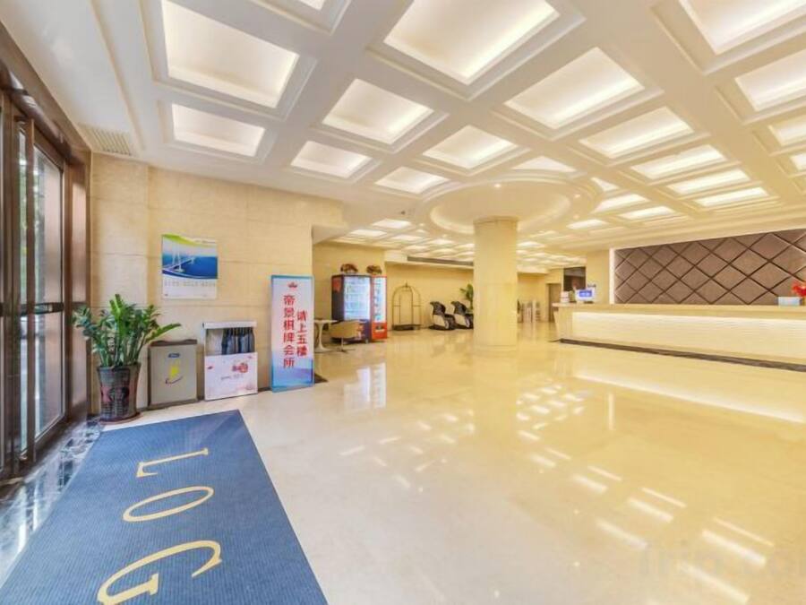 A hotel reception area with a reception desk, a blue carpet with 'LOG' text, a large window, and a wall-mounted TV.