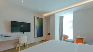 Quarto de hotel moderno com uma cama grande, televisão de tela plana na parede, escrivaninha pequena com cadeira e janela com cortinas.