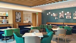Um restaurante moderno com assentos verdes e cinzentos, um cozinheiro ao fundo e uma parede decorada com quadros.