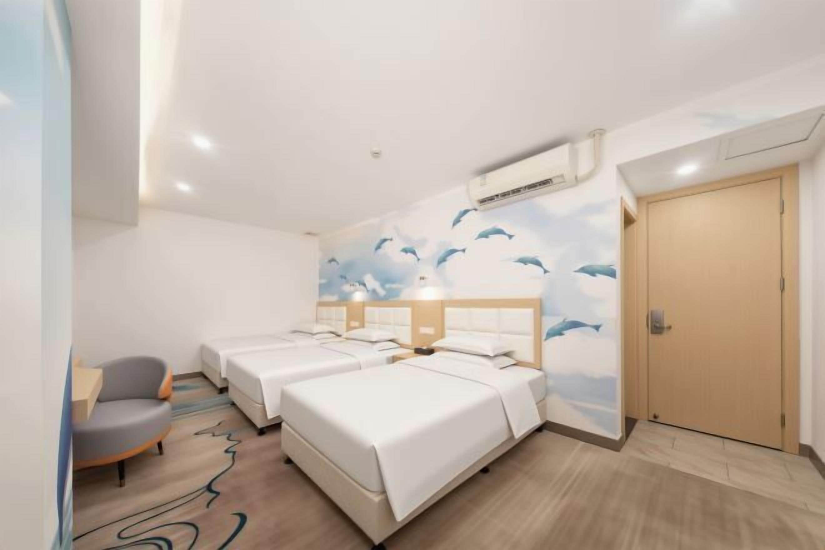 A hotel room with two beds, a desk, a chair, and a mural of dolphins.