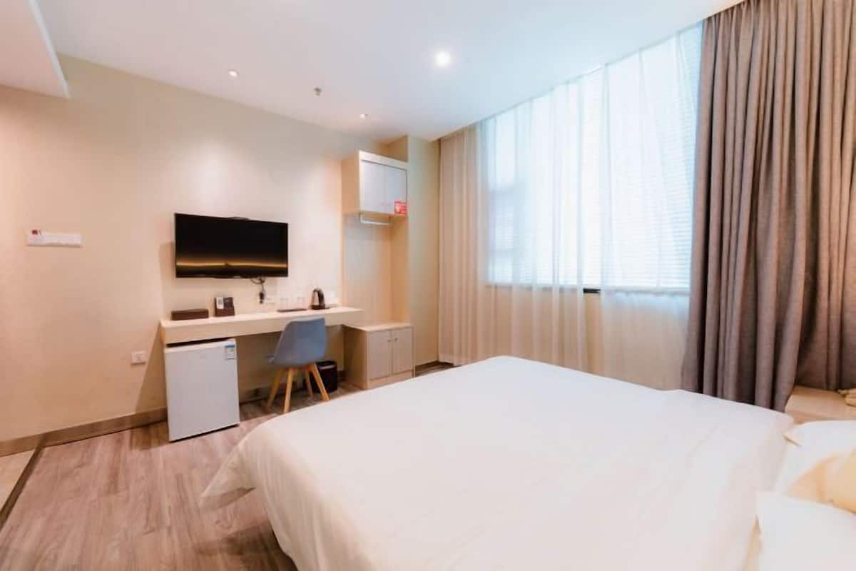A hotel room with a bed, a desk, a television, and a window with curtains.