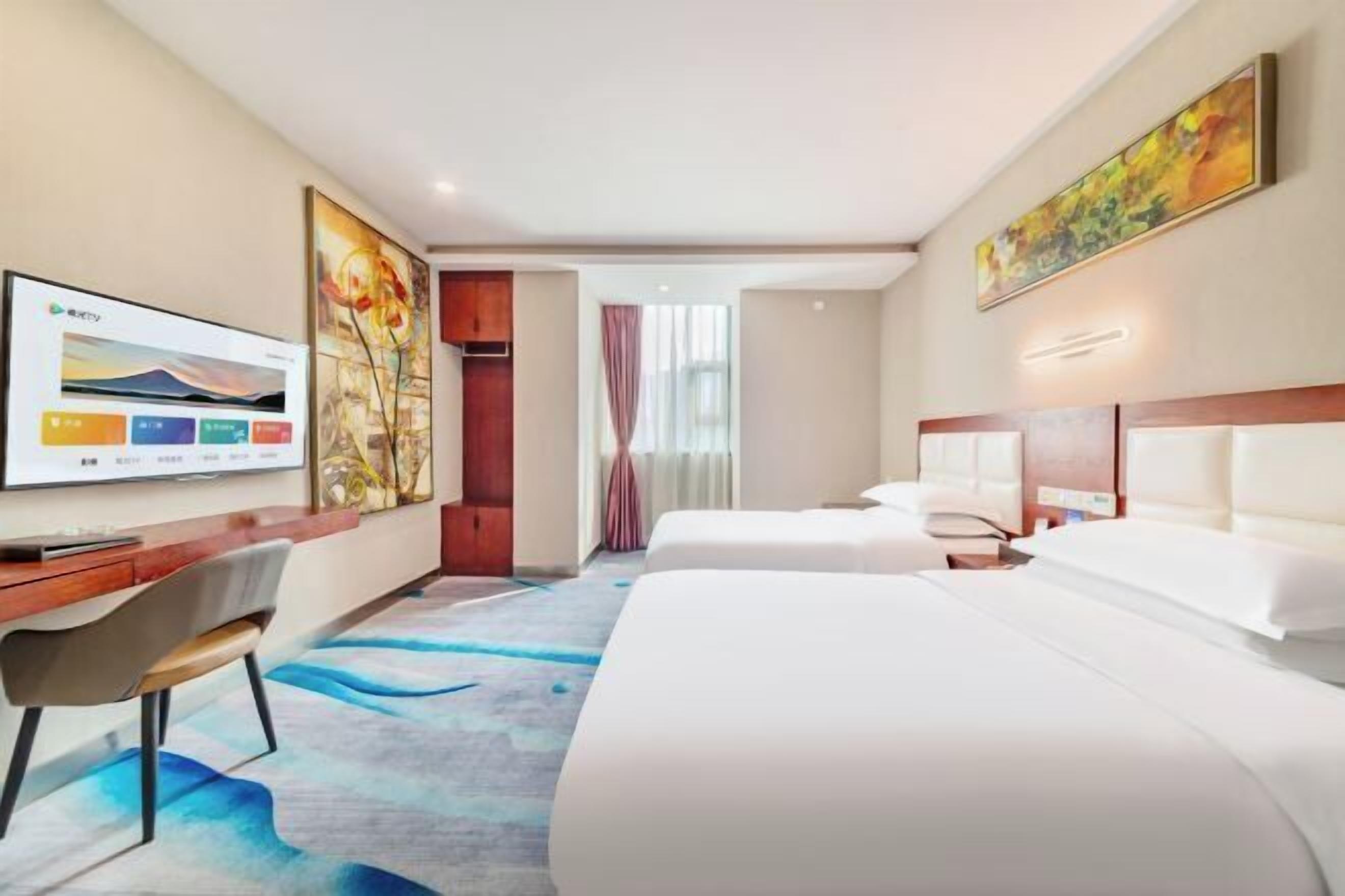A hotel room with two beds, a desk, a chair, a TV, and artwork on the walls.