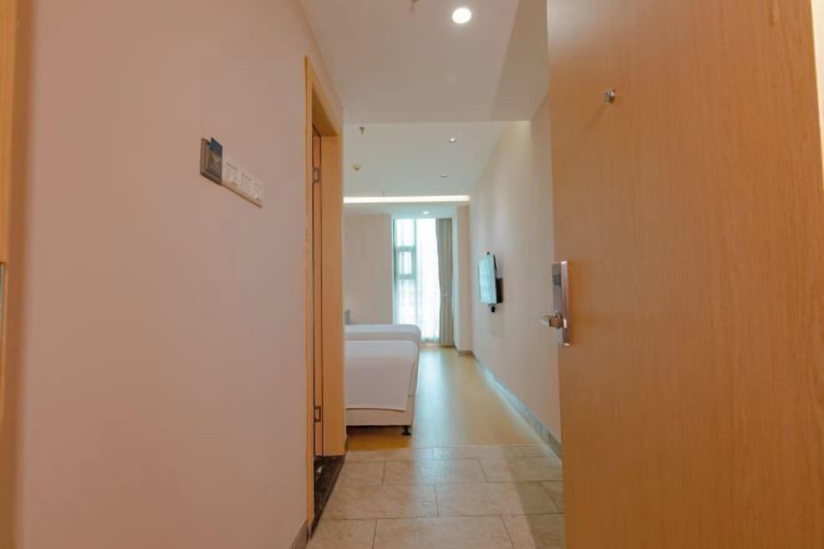 A hotel hallway with a bed, a door, and a light fixture on the wall.
