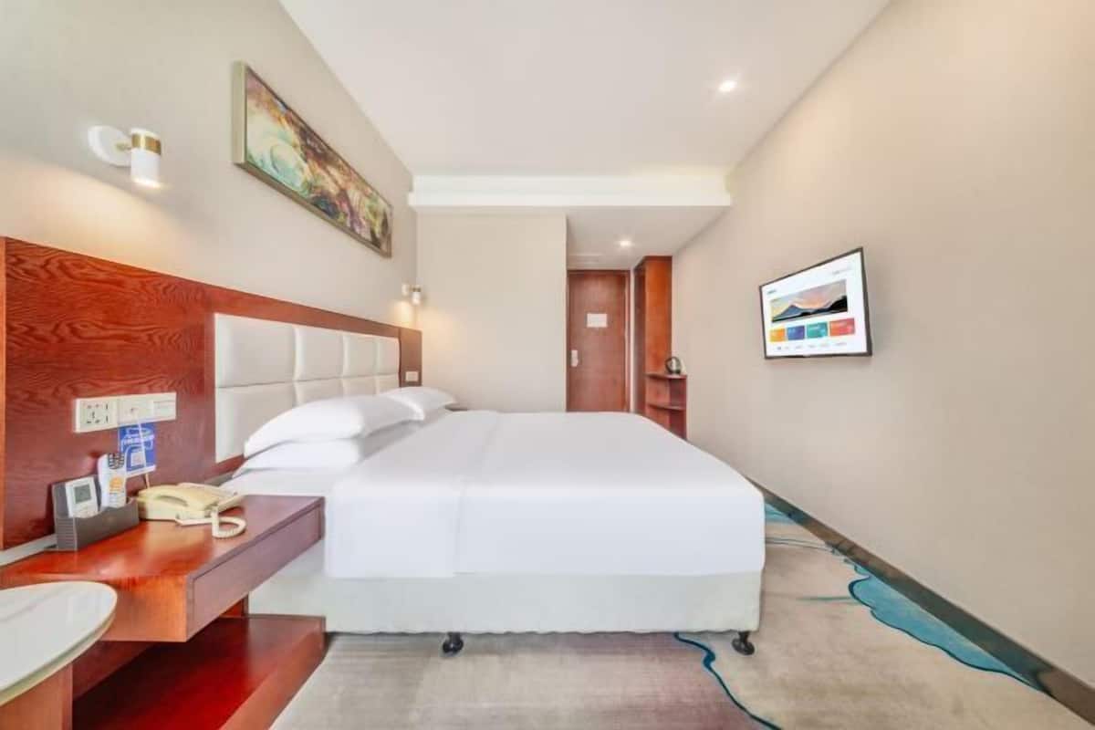 A hotel room with a bed, bedside table, phone, and a painting on the wall.