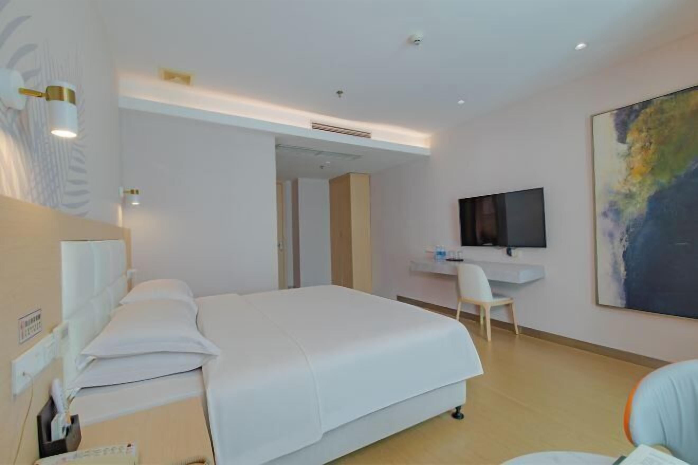 Ein Hotelzimmer mit einem Bett, einem Schreibtisch, einem Sessel, einem Fernseher und einem Bild an der Wand.