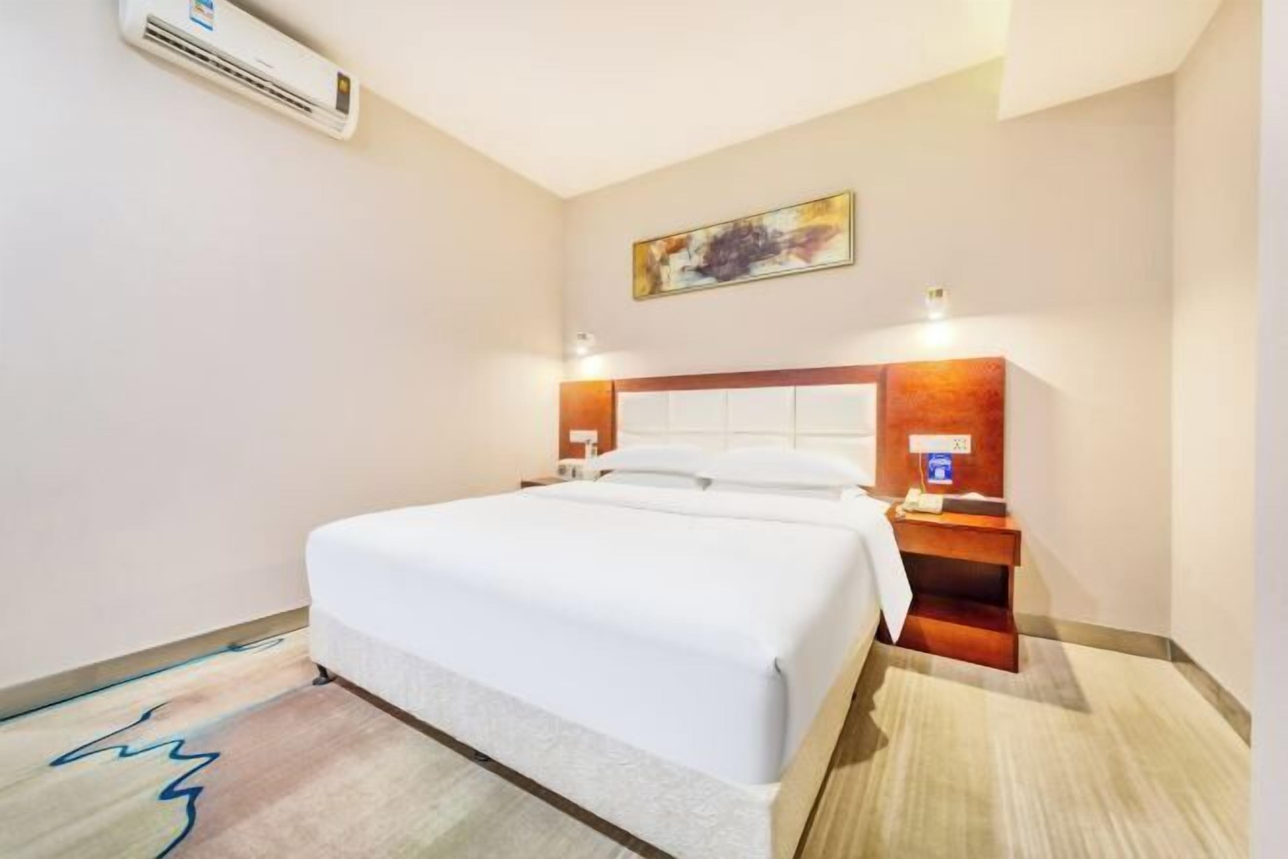 Habitación de hotel con una cama grande, una mesita de noche, un aire acondicionado de pared y un cuadro sobre la cama.