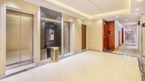 Corredor de hotel com piso lustroso, balcão de recepção e placa indicando a direção dos elevadores.
