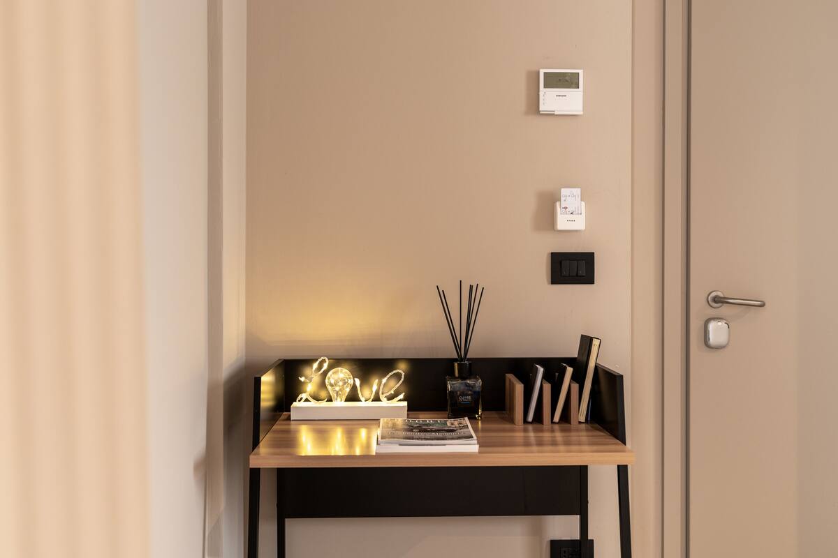 Ein Hotelrezeptionstresen mit einem beleuchteten 'LOVE'-Schild, einem digitalen Thermostat und einem kleinen Tisch mit Büchern und einer Kerze.