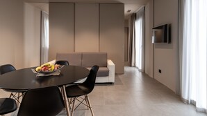 Una habitación de hotel moderna con una mesa de comedor, sillas, un sofá y un televisor de pantalla plana montado en la pared.