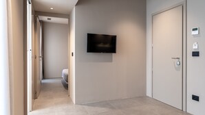 Un pasillo con una televisión de pantalla plana montada en la pared, una puerta con manija y un termostato en la pared.