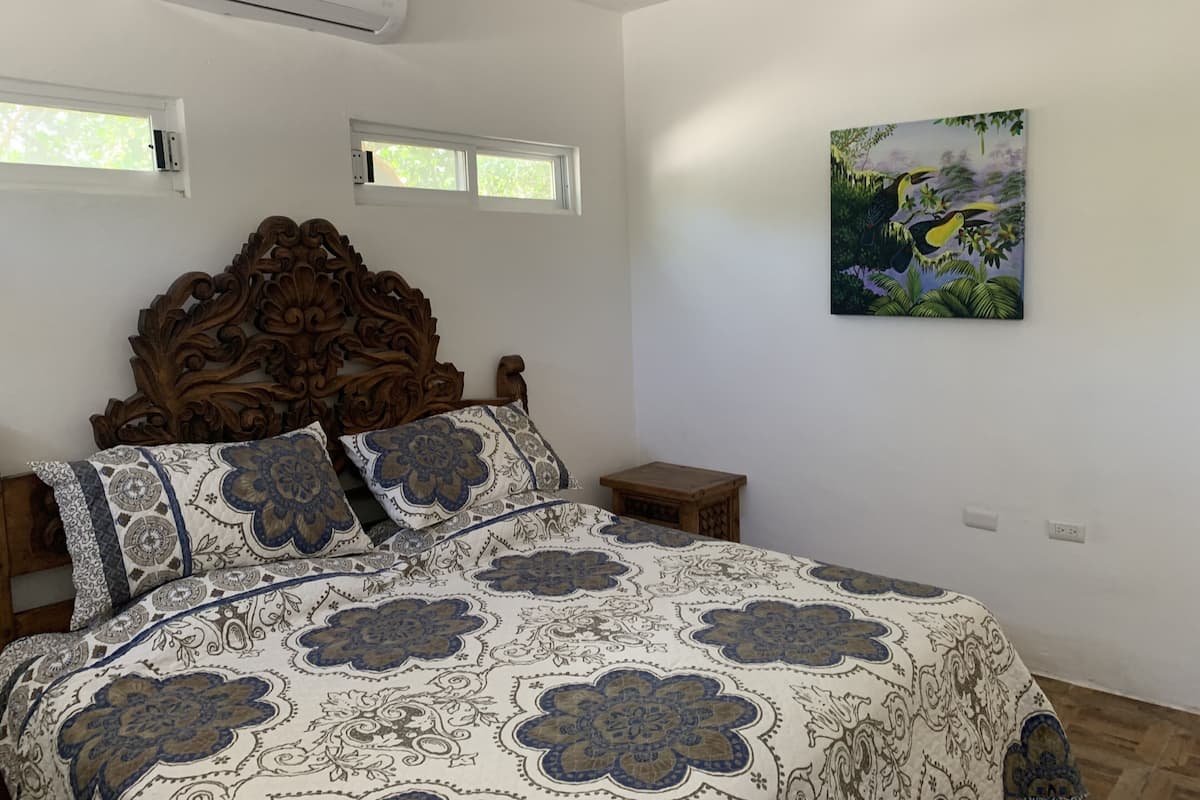 A bedroom with a wooden headboard, a patterned bedspread, two bedside tables, and a wall-mounted painting.