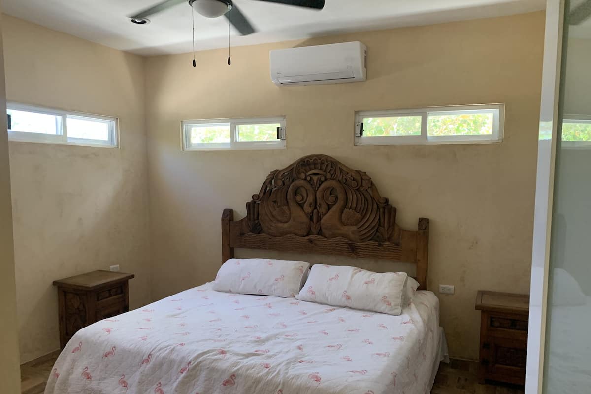 A bedroom with a large bed, two nightstands, a ceiling fan, and three windows.