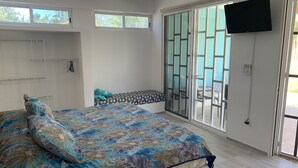 A bedroom with a bed, a ceiling fan, a TV, and a sliding glass door to the outside.