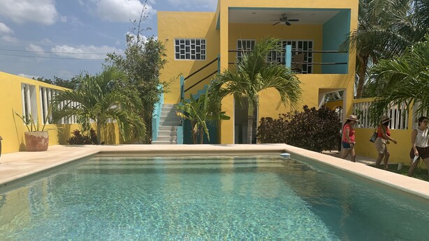 A clear swimming pool with a yellow building in the background, a staircase, and some greenery.