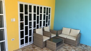 A room with a yellow and blue wall, a sliding glass door, wicker furniture, and a tiled floor.