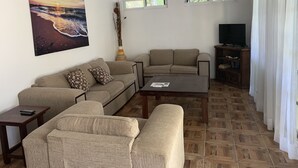 A living room with a sofa, armchairs, a coffee table, a TV, and a bookshelf.