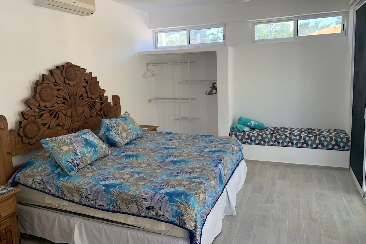 A bedroom with a large bed, a wooden headboard, a ceiling fan, a window, and a built-in bench.