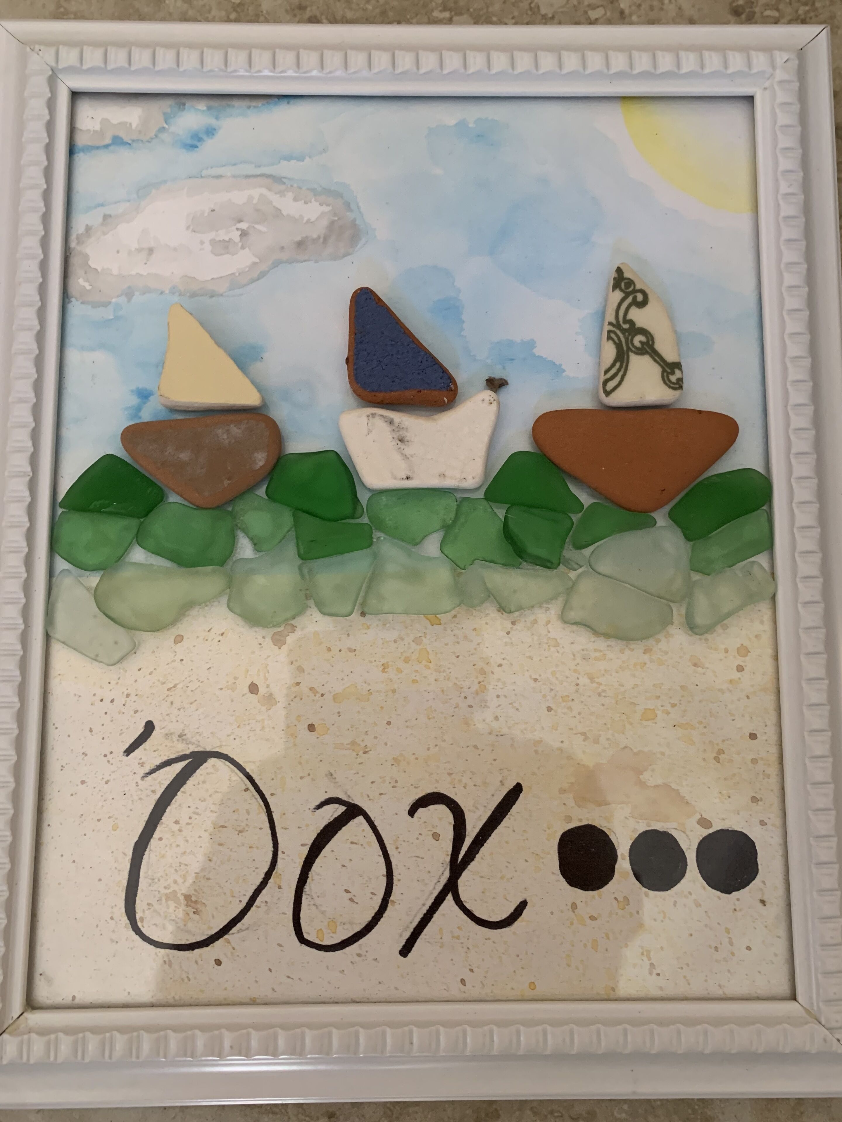 A framed artwork with a beach scene, including a sun, clouds, and a wave.