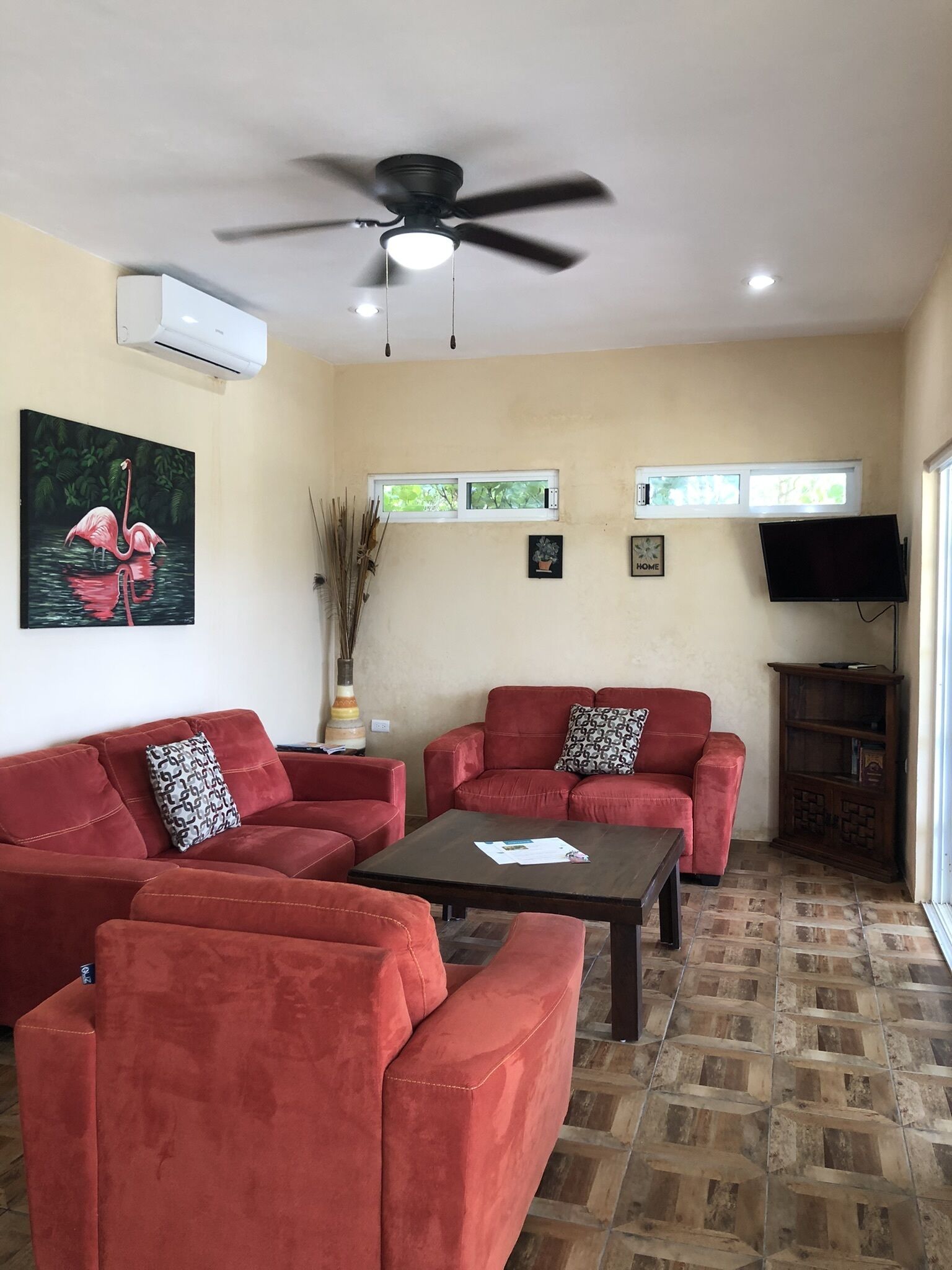 A living room with red sofas, a coffee table, a ceiling fan, and a TV on a wooden cabinet.