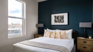 A bedroom with a large bed, two bedside tables, a window, and a wall-mounted artwork.