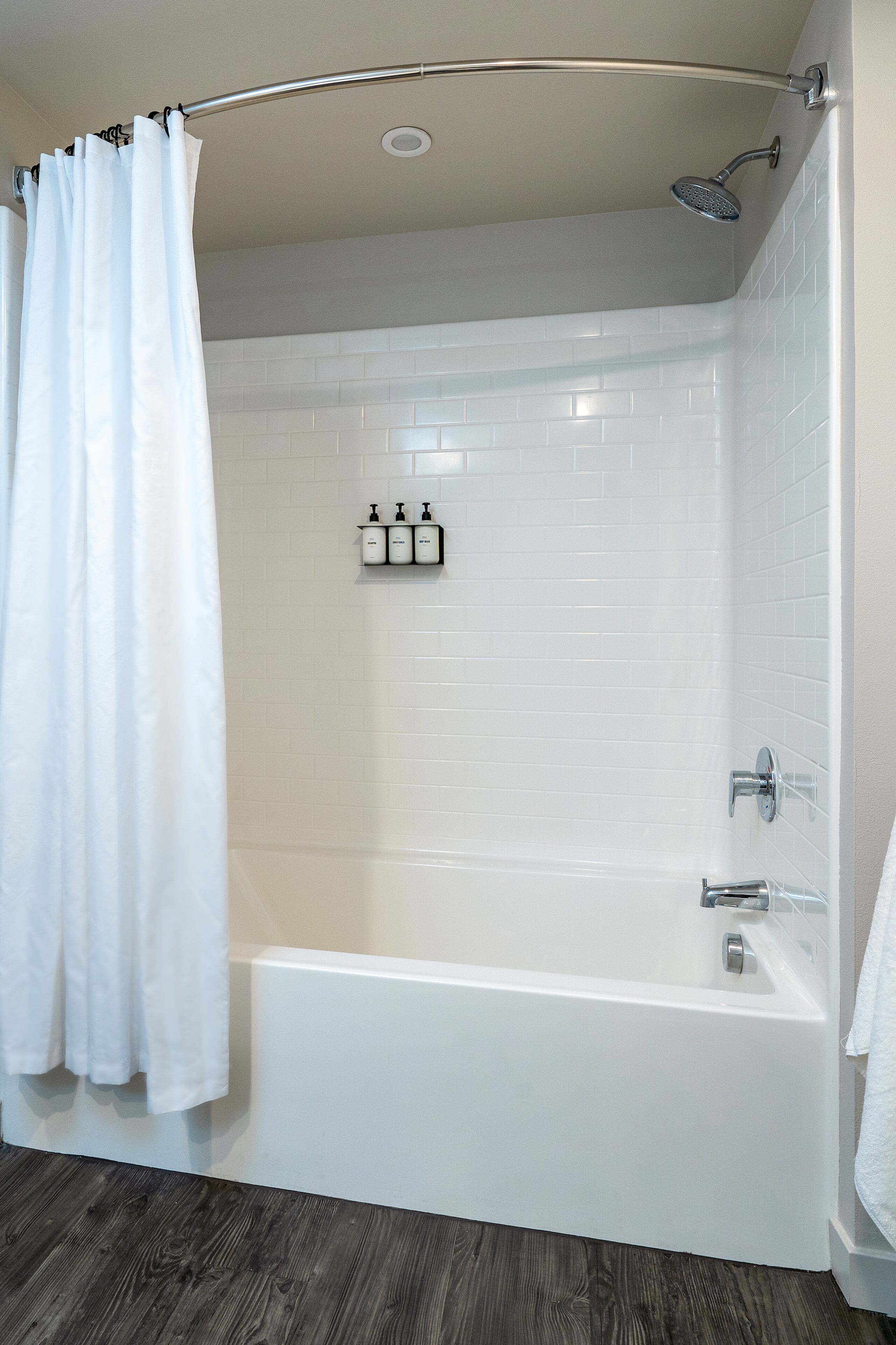 A modern bathroom with a white bathtub, a showerhead, and a towel rack with bottles.
