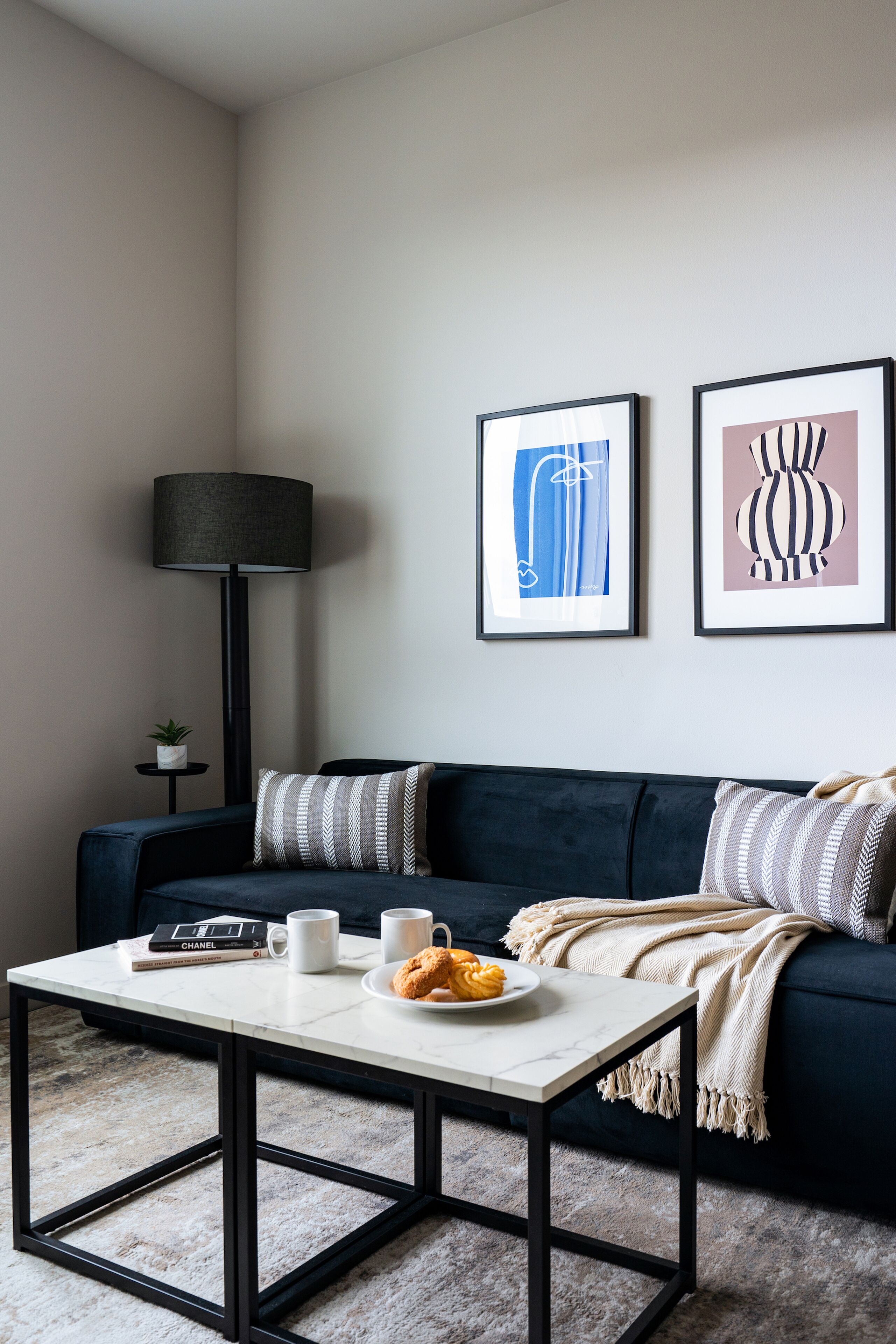 A modern living room with a dark blue sofa, a white coffee table, and two framed abstract artworks on the wall.