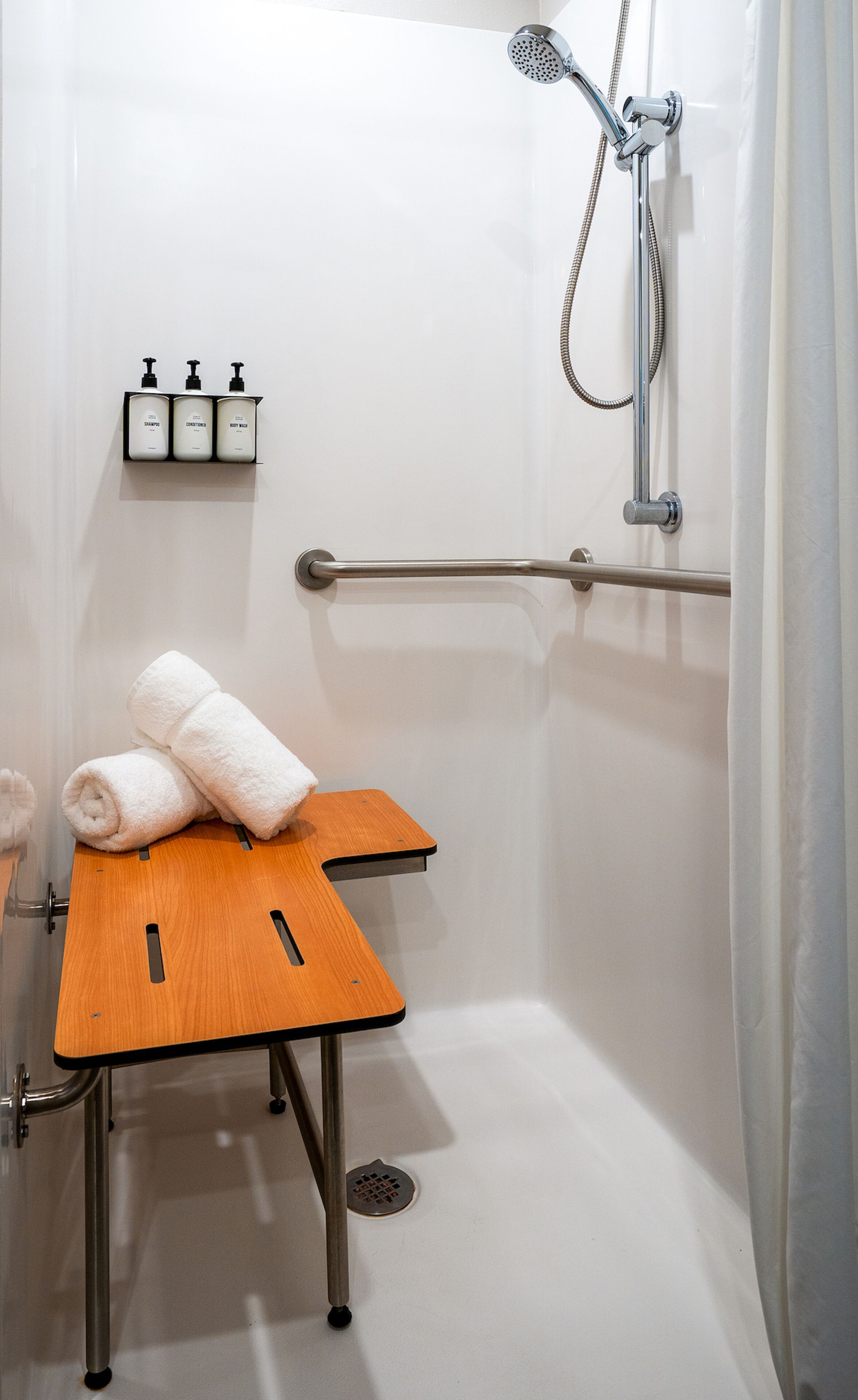 A modern shower area with a handheld showerhead, a grab bar, and a small wooden table with towels.