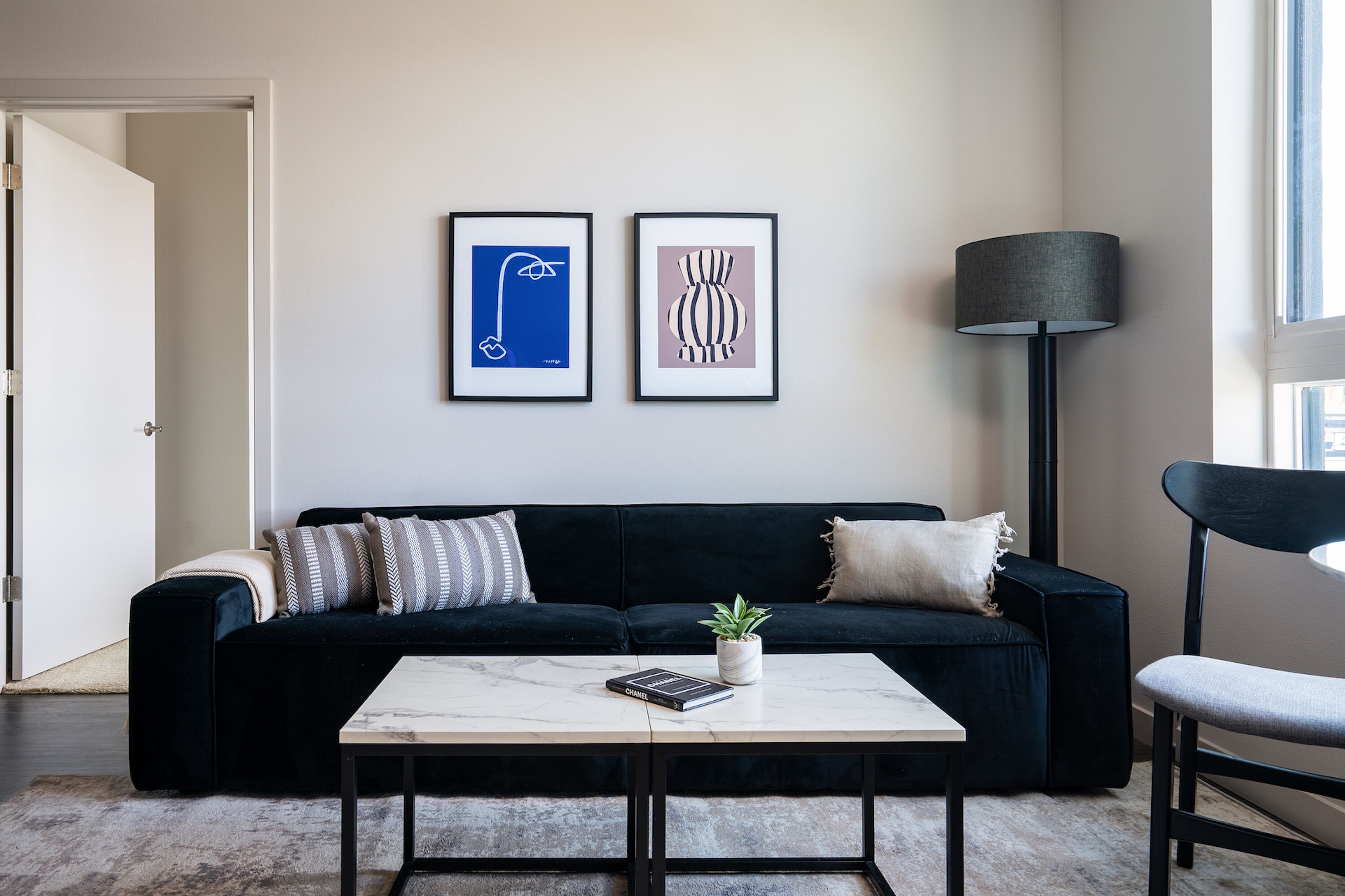 Una sala moderna con un sofá oscuro, una mesa de centro blanca y dos obras de arte enmarcadas en la pared.