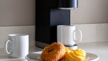 A modern coffee maker on a countertop with two white mugs and a plate with pastries.