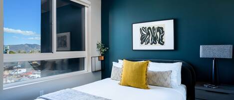 A bedroom with a large bed, a view of the mountains through a window, and a dark blue accent wall.