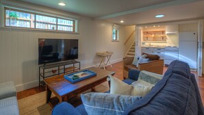 A living room with a TV, sofa, and coffee table. A kitchen is visible in the background. - Dog-Friendly Cottage with hot tub, kayaks, e-bike (Eastsound)