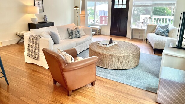 A spacious living room with a large window, a sofa, a coffee table, and a chair. - Dog-Friendly Cottage with hot tub, kayaks, e-bike (Eastsound)