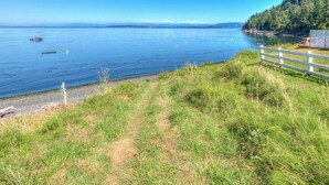 A serene lakeside view with a wooden fence, grassy area, and a distant mountain range. - Dog-Friendly Cottage with hot tub, kayaks, e-bike (Eastsound)