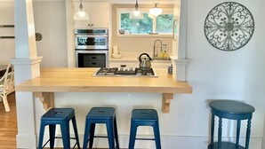 A kitchen with a central island, three stools, a stove, and a window with a view of greenery. - Dog-Friendly Cottage with hot tub, kayaks, e-bike (Eastsound)