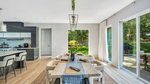 Une cuisine moderne avec un coin repas, de grandes fenêtres et une vue sur une forêt.