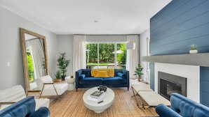 Un salon moderne avec un canapé bleu, des fauteuils blancs, une table basse et une cheminée.
