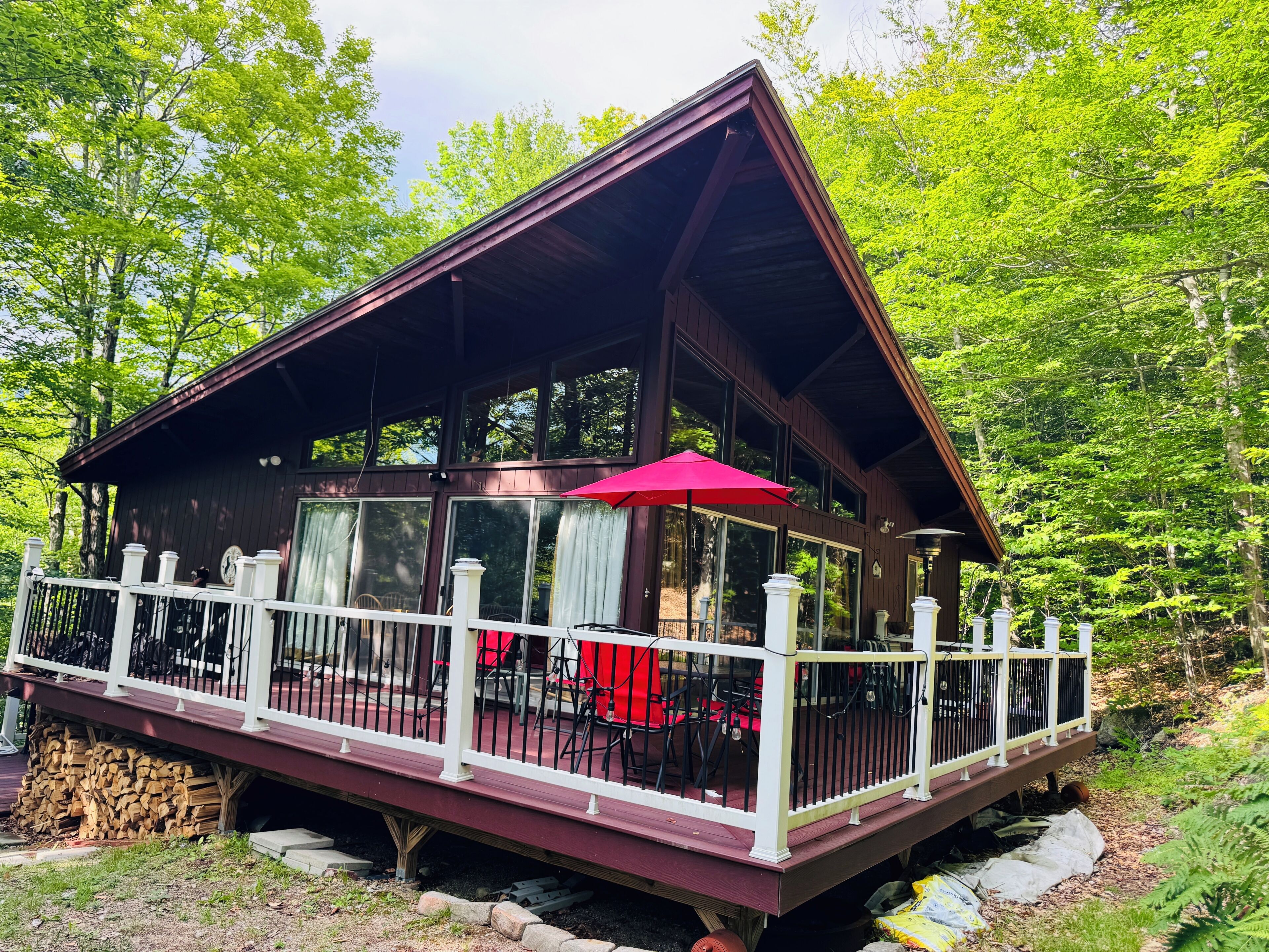 Eine Holzhütte mit überdachter Terrasse, großen Fenstern und einem roten Regenschirm.