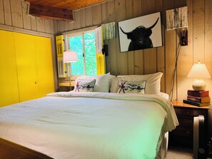 A bedroom with a bed, pillows, a bedside lamp, and a window with shutters.
