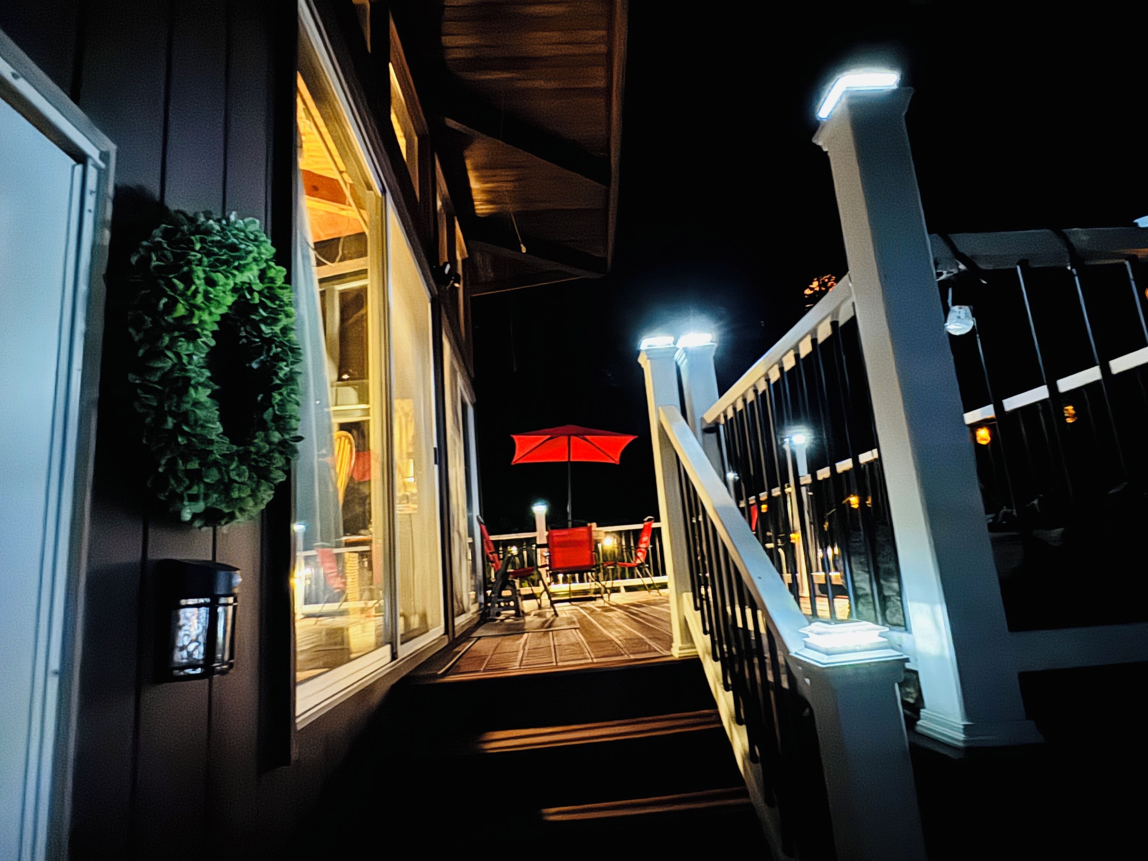 A staircase leading to a deck area with outdoor seating, a red umbrella, and a wreath on the wall.