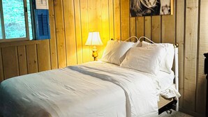 A wooden-paneled room with a bed, a window, and a lamp.