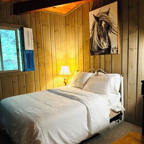 Une pièce aux murs lambrissés, avec un lit, une fenêtre et une lampe.