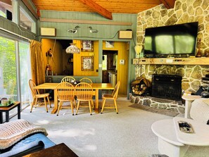 A cozy interior with a dining area, a stone fireplace, and a television mounted above it. - Family size Cabin w deck, Resort Pool &Spa walk to gondola & Scottish Festival  (Lincoln)