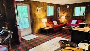 Interior acolhedor de uma cabana com piso xadrez, um sofá vermelho, uma mesa de jantar de madeira e uma lareira.