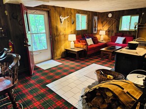 Ein gemütliches Blockhäuschen-Interieur mit kariertem Boden, einem roten Sofa, einem Holzespeise-Tisch und einem Kamin.