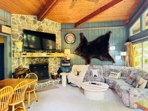 Ein gemütliches Wohnzimmer mit Kamin aus Stein, einem Wand-Fernseher, einer großen Ledercouch und einem sofa mit Muster.