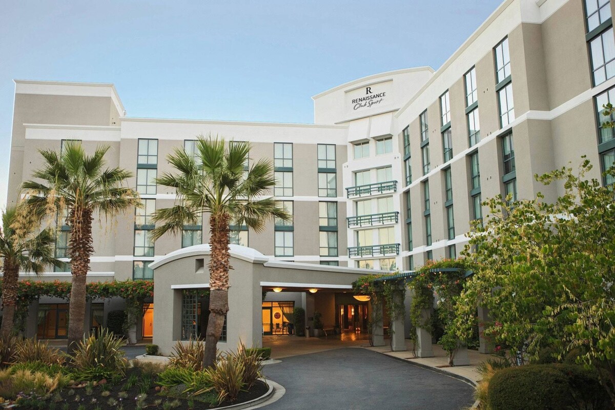 A multi-story hotel with a central entrance, palm trees, and a well-maintained garden.