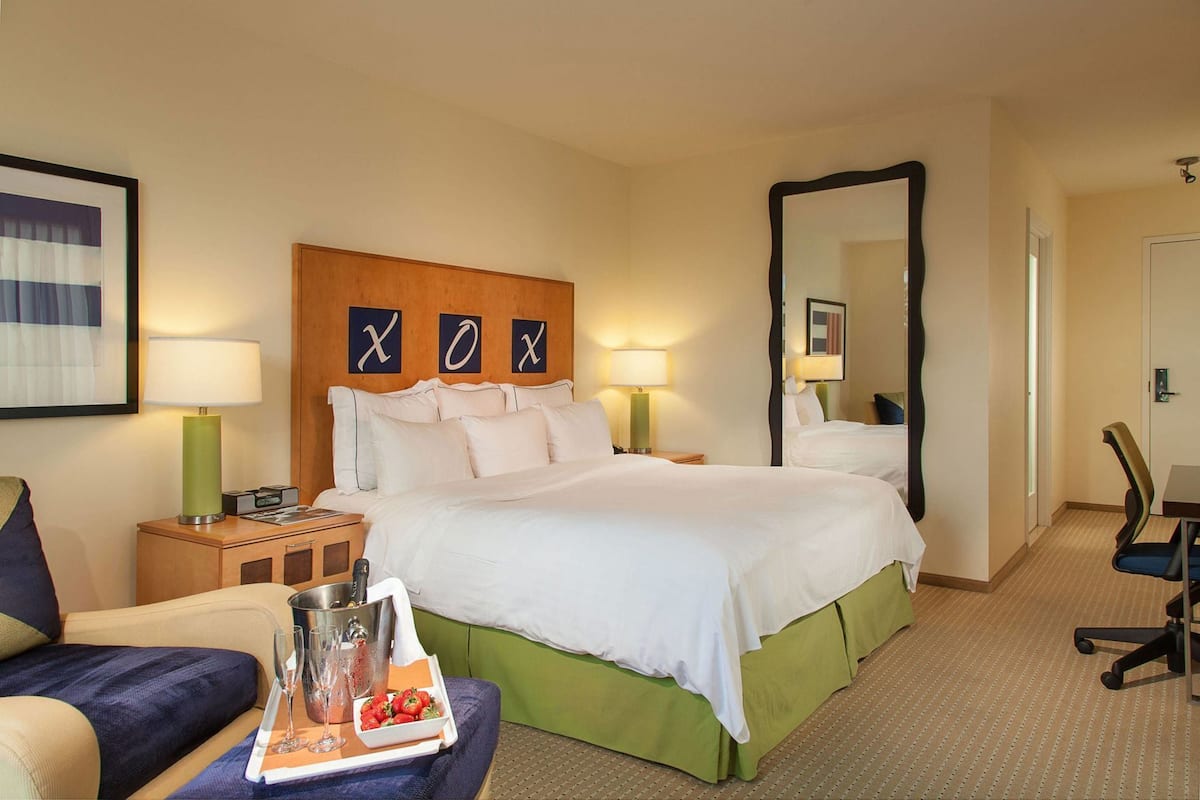 A hotel room with a large bed, two bedside tables with lamps, a chair, a desk, and a mirror.